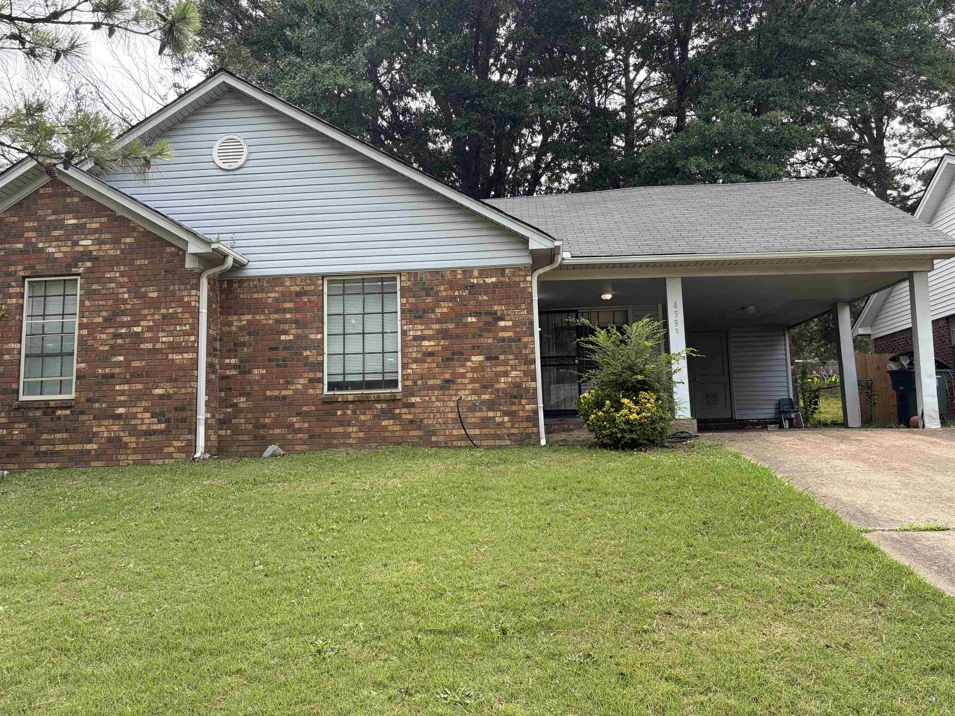 Brick and siding exterior featuring a covered carport, pitched roof, and mature perimeter trees