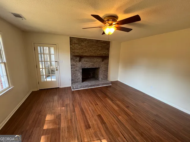 an empty room with wooden floor fireplace and windows