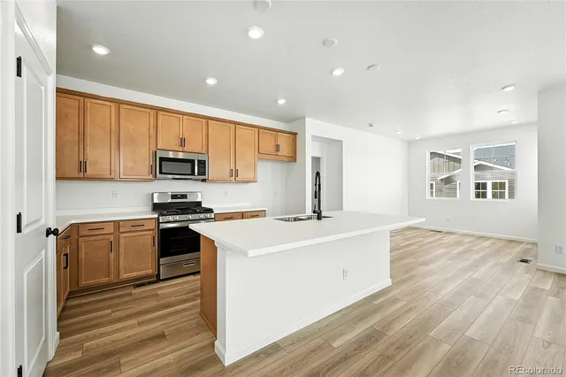 a kitchen with stainless steel appliances granite countertop a stove a sink a refrigerator white cabinets and wooden floor