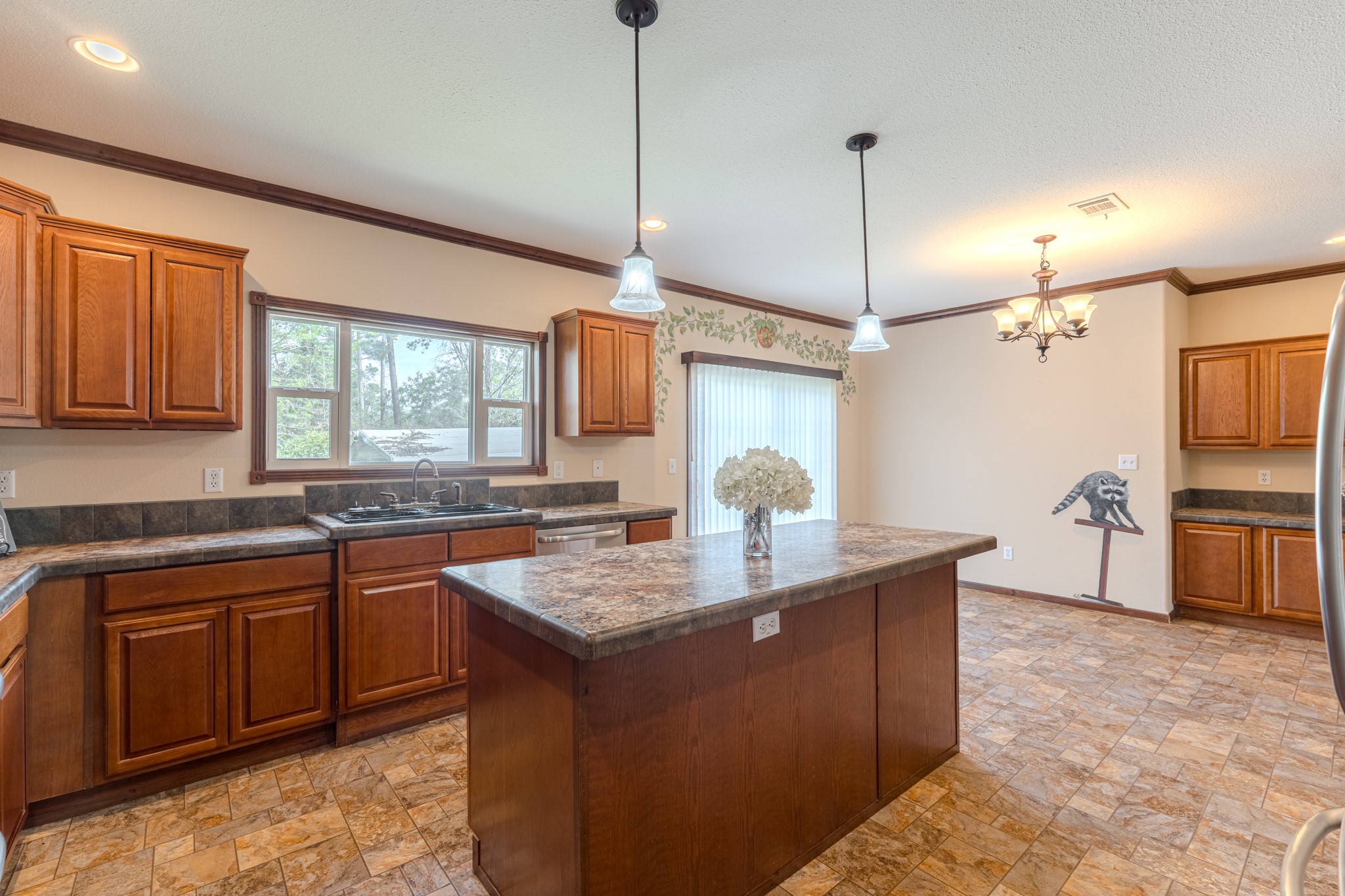 115 Canadian Drive Trinity, TX 75862 - Photo 12 of 42 Notice the modern pendant lighting . It includes a window over the sink for natural light, a decorative wall border, and a cozy dining area with a chandelier.