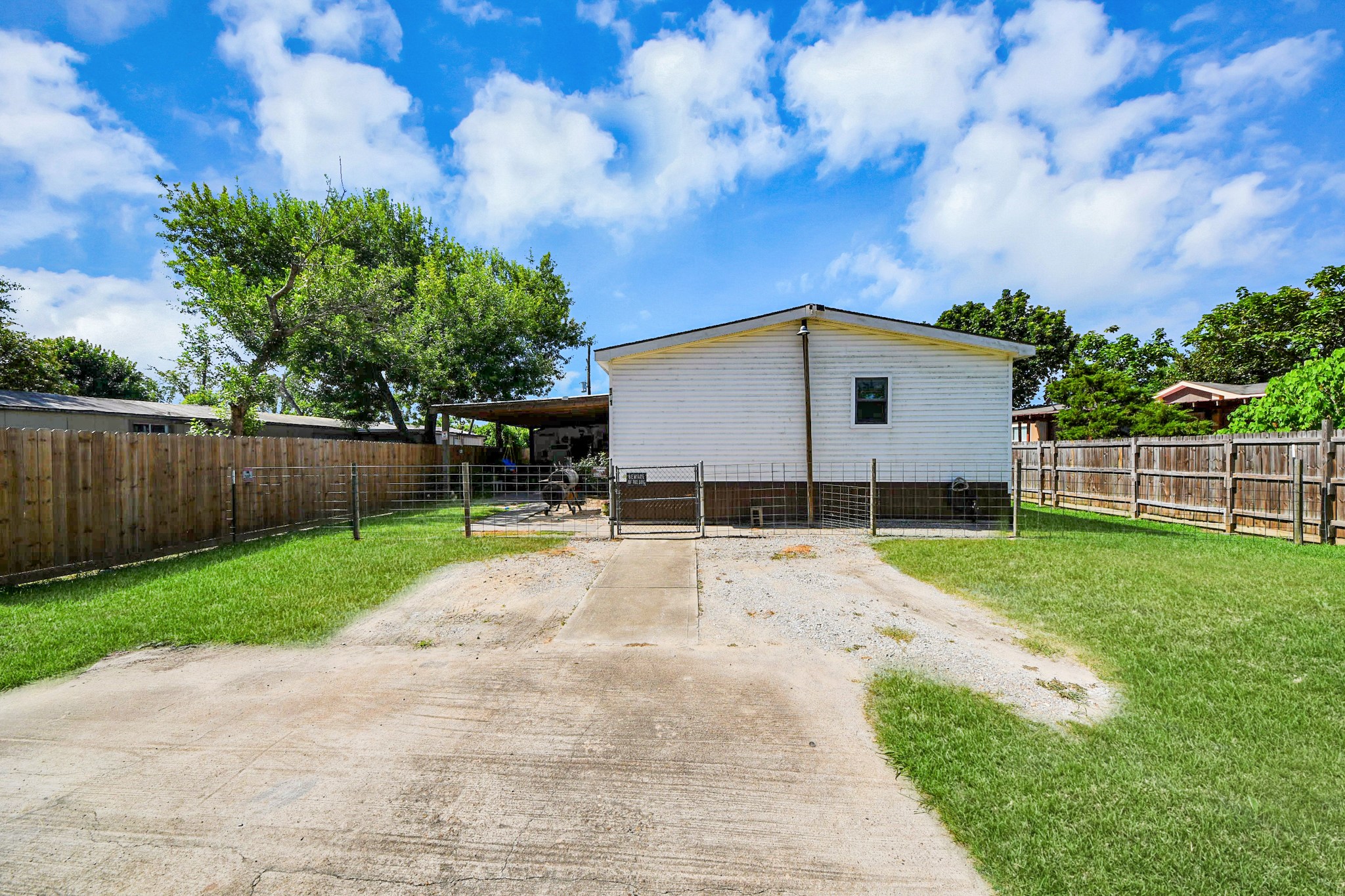 131 Kiowa Court Rosharon, TX 77583 - Photo 2 of 42 The back of the house with a fenced yard, a covered patio area, and a spacious driveway. The yard is mostly grass with a few trees, providing a private outdoor space.