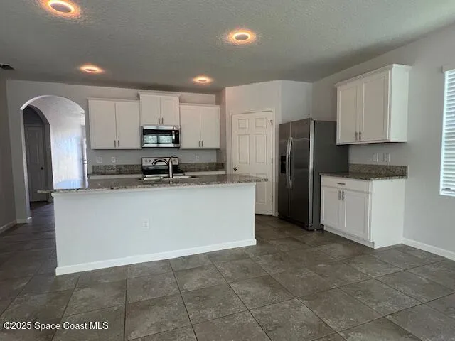 a kitchen with stainless steel appliances granite countertop a refrigerator a stove a sink and white cabinets