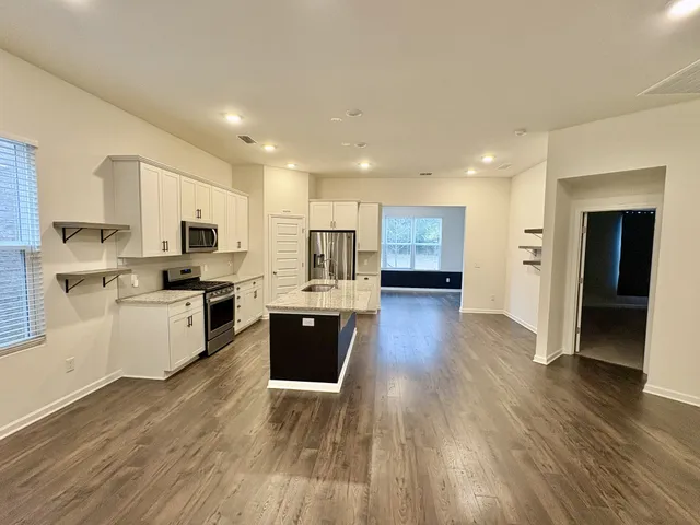 a kitchen with stainless steel appliances granite countertop a stove top oven a sink dishwasher and a refrigerator with wooden floor