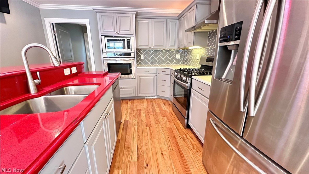 2603 Rockefeller Road Wickliffe, OH 44092 - Photo 7 of 34 Kitchen featuring bright red countertops, light-toned wood-finish flooring, stainless steel appliances, grey cabinetry, and a herringbone tile backsplash