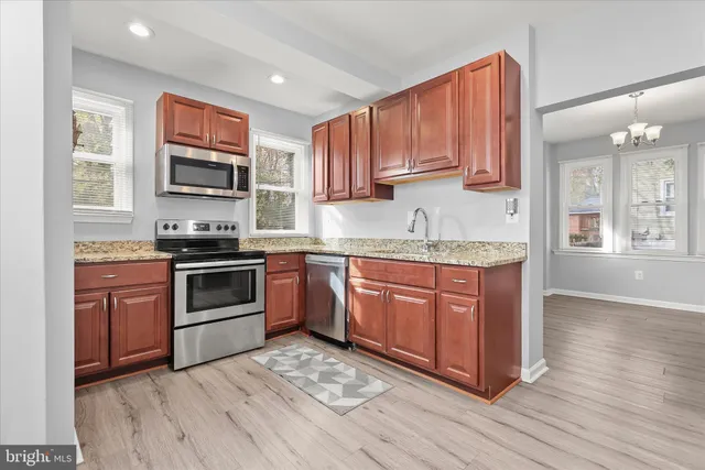 a kitchen with stainless steel appliances granite countertop a stove top oven a sink dishwasher and a microwave oven on the wooden floor