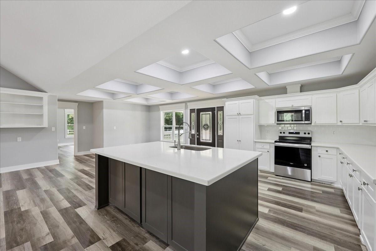 8679 Massey Lake Road Silsbee, TX 77656 - Photo 18 of 37 a large white kitchen with kitchen island a stove a sink a refrigerator and white cabinets with wooden floor