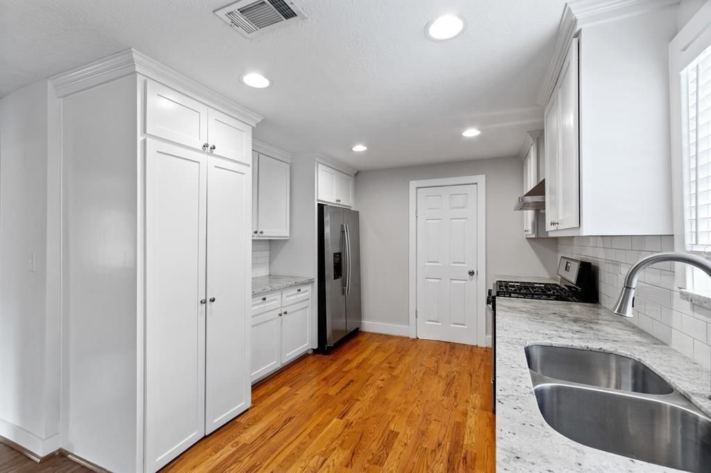 1305 Idylwild Street Houston, TX 77009 - Photo 11 of 31 This kitchen features sleek white cabinetry, stainless steel appliances, and granite countertops. It has warm hardwood flooring, ample storage, and modern recessed lighting.