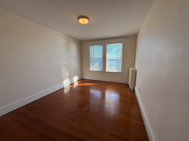 an empty room with wooden floor and windows with curtains
