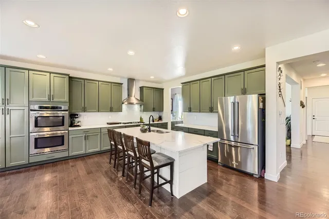 a kitchen with stainless steel appliances granite countertop a refrigerator a stove a sink a microwave and a dining table with wooden floor