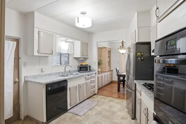 a kitchen with stainless steel appliances granite countertop a stove top oven a sink a refrigerator white cabinets and wooden floor