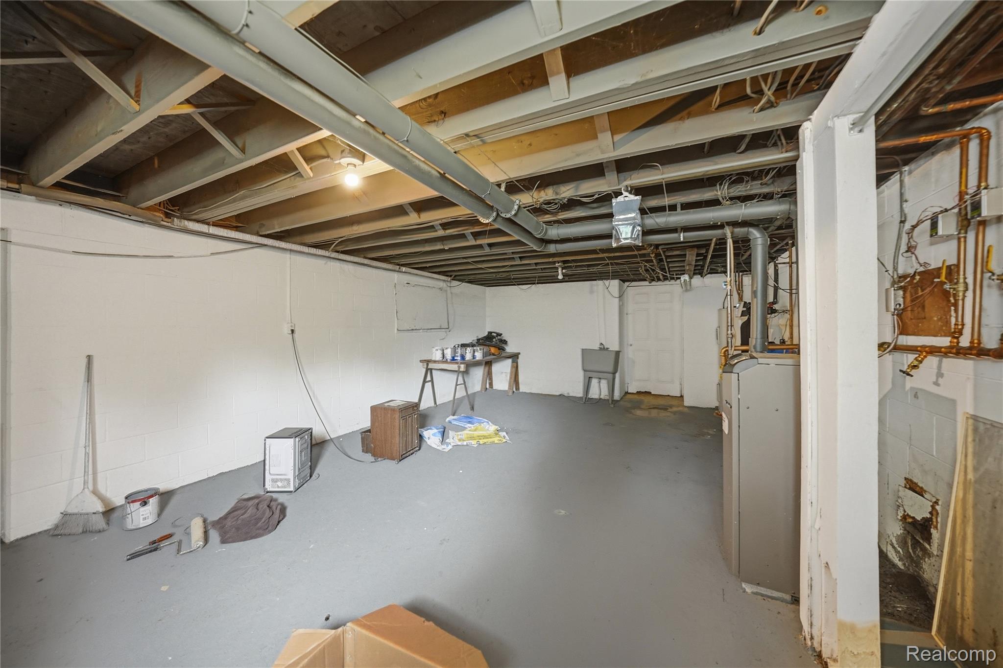 6790 Weyer Road Imlay City, MI 48444 - Photo 27 of 34 Unfinished basement featuring exposed ceiling joists, painted concrete block walls, painted concrete flooring, an exposed utility sink, and a water heater