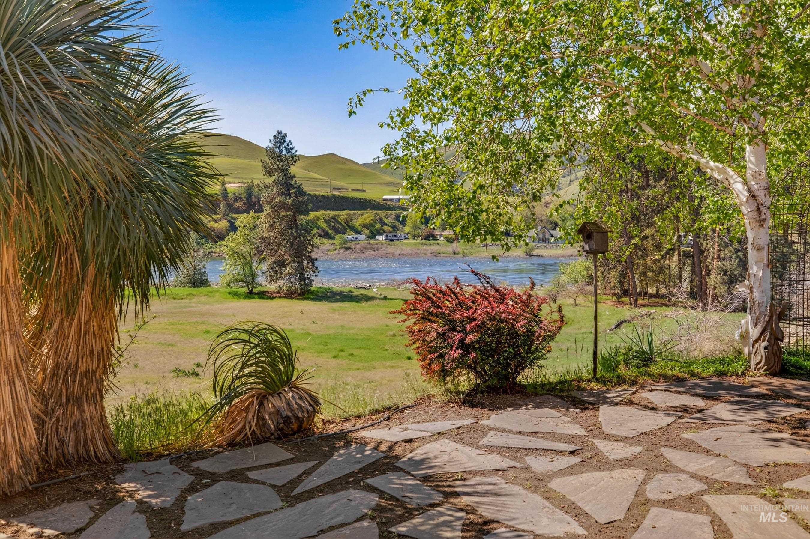113 Deford Road White Bird, ID 83554 - Photo 32 of 49 Stone patio with irregular flagstone pavers, surrounded by mature trees and shrubs, overlooking a body of water with distant rolling hills