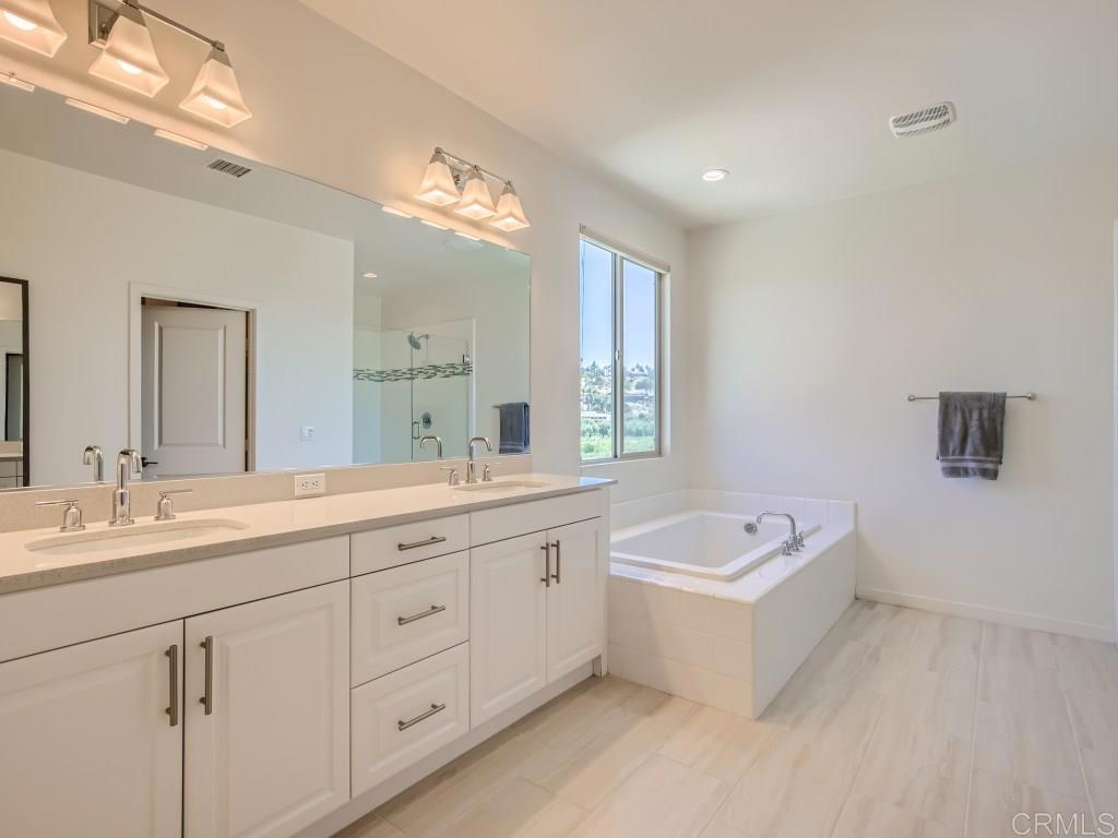 31657 Calle De Las Estrellas Bonsall, CA 92003 - Photo 16 of 24 a spacious bathroom with a double vanity sink large mirror bathtub and window
