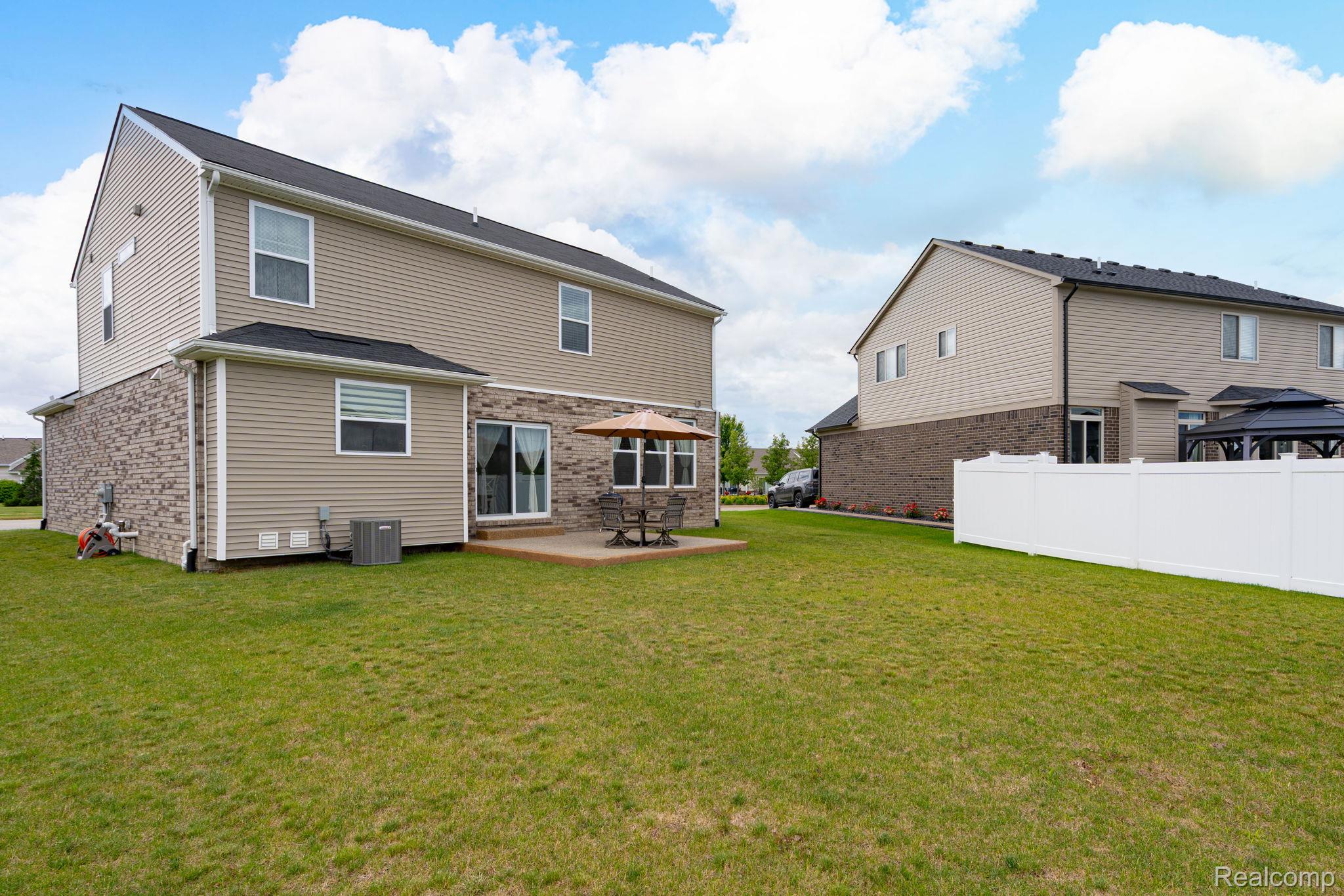 48904 Carnegie Way Macomb, MI 48042 - Photo 4 of 34 Expansive backyard featuring a manicured lawn, a concrete patio, and a white privacy fence