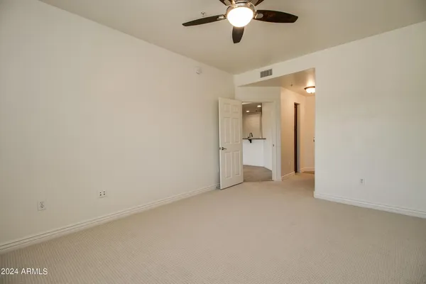 an empty room with chandelier fan and kitchen view