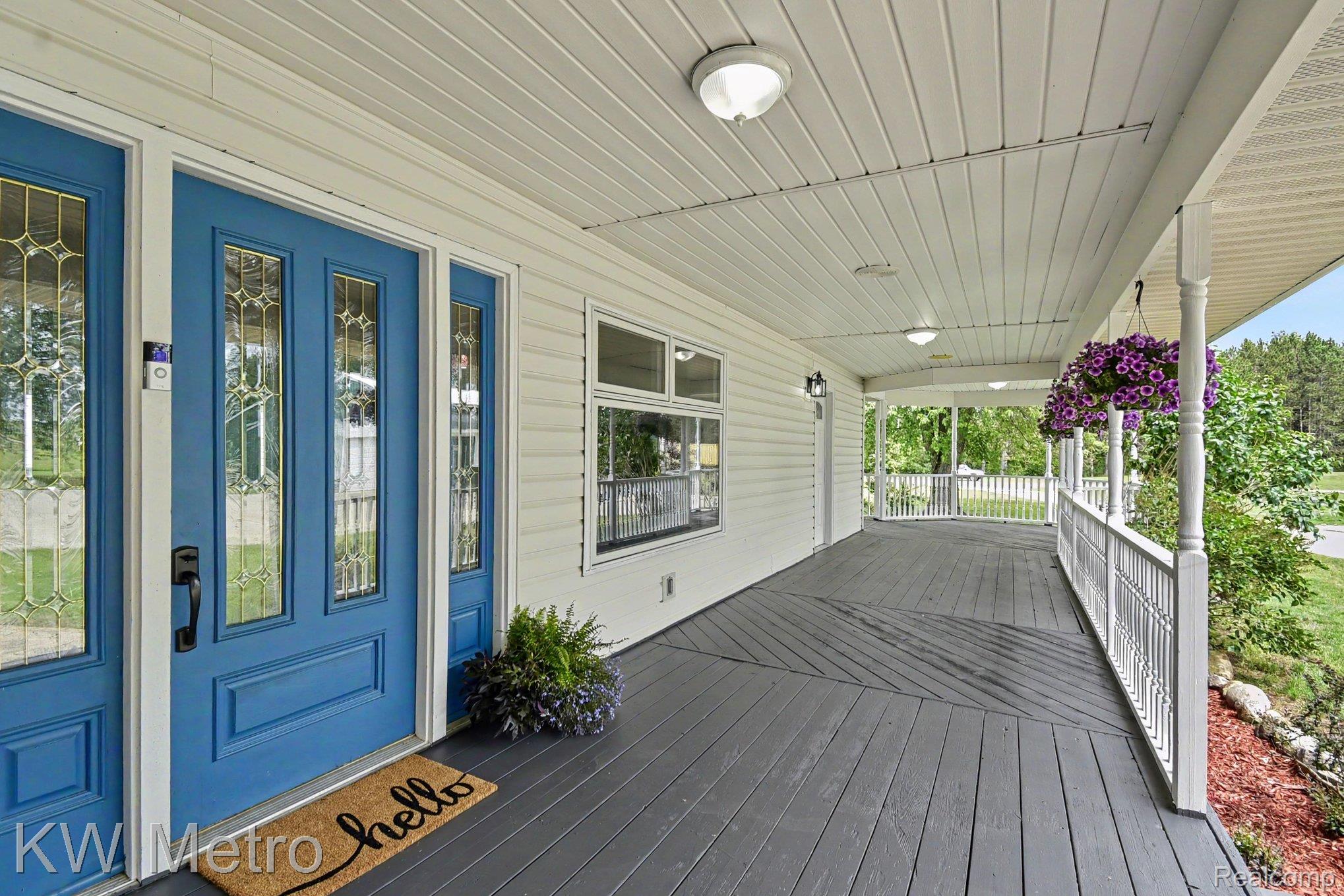 2682 East Haskell Lake Road Harrison, MI 48625 - Photo 9 of 61 Expansive covered front porch with gray wood-finish flooring, white siding, and a vibrant blue entry door with decorative glass panels