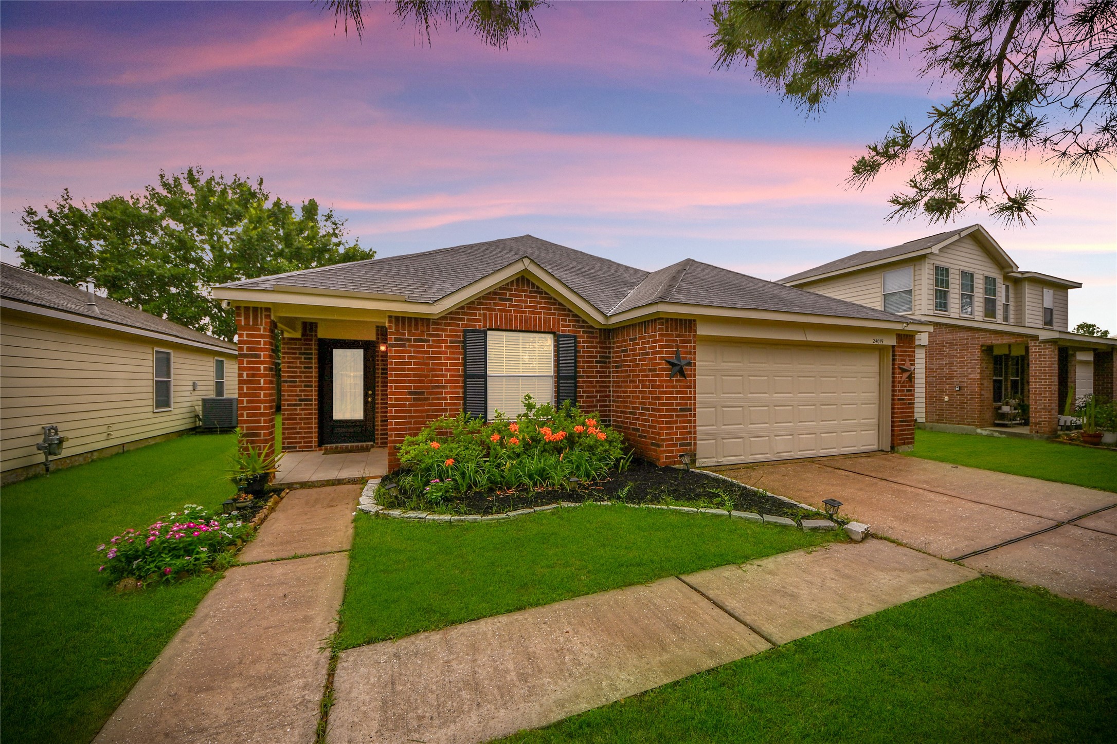 24019 Kingbriar Drive Spring, TX 77373 - Photo 1 of 41 This striking twilight exterior photograph captures the elegant brick facade and impeccable landscaping against a vibrant sky, emphasizing the home’s inviting and beautiful evening presence.