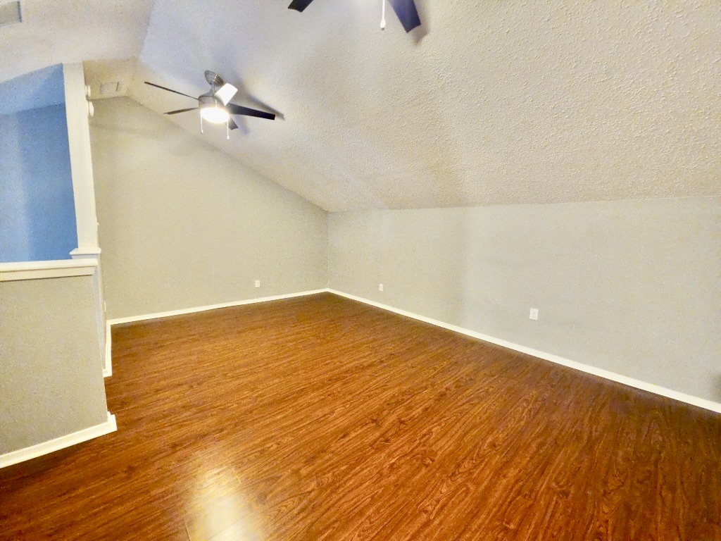 2500 Burleson Road, Unit 521 Austin, TX 78741 - Photo 11 of 20 Spacious room featuring rich wood-finish flooring, a sloped ceiling, and a ceiling fan with integrated lighting
