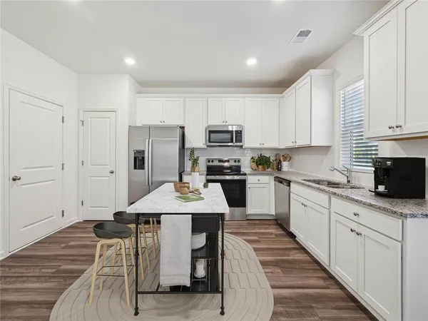 a kitchen with stainless steel appliances granite countertop a refrigerator a stove top oven a sink dishwasher and white cabinets with wooden floor