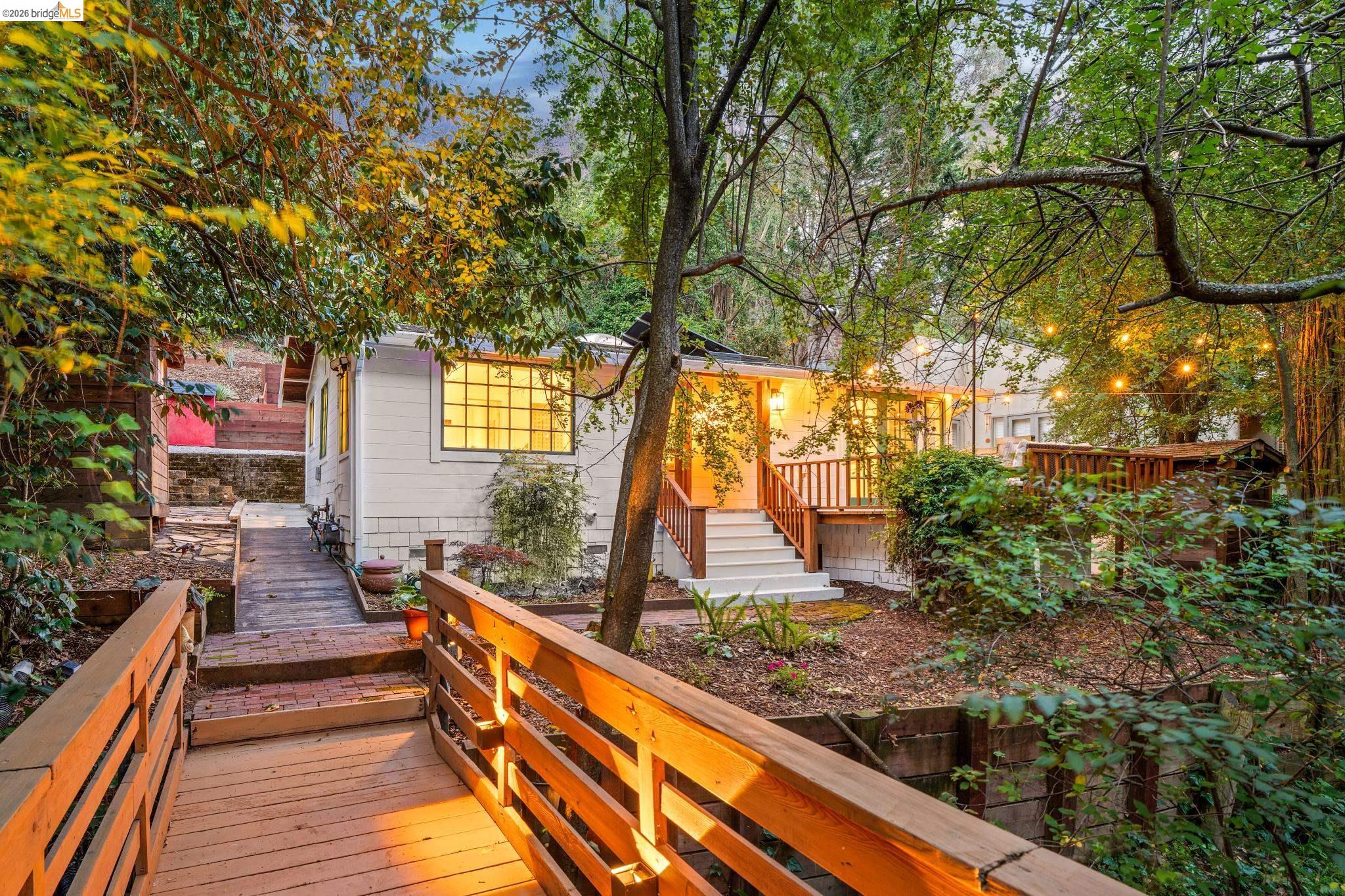 6400 Pinehaven Road Oakland, CA 94611 - Photo 1 of 78 Wood-finish walkway with railings leading to a white exterior home featuring a terraced landscape with mature trees and established plantings