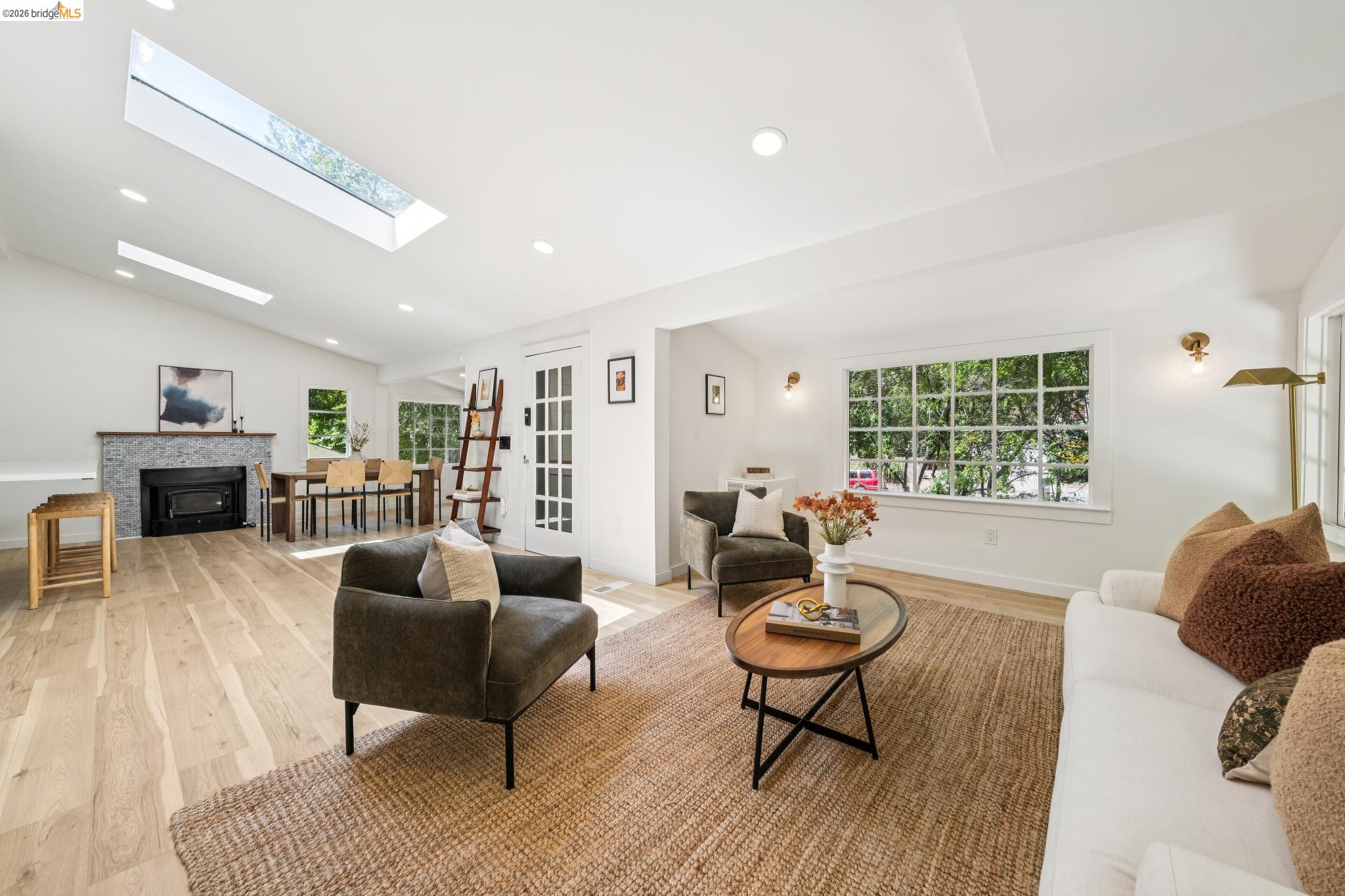 6400 Pinehaven Road Oakland, CA 94611 - Photo 11 of 78 Spacious open-concept living area featuring wood-finish flooring, a contemporary fireplace with a stone surround, and multiple skylights