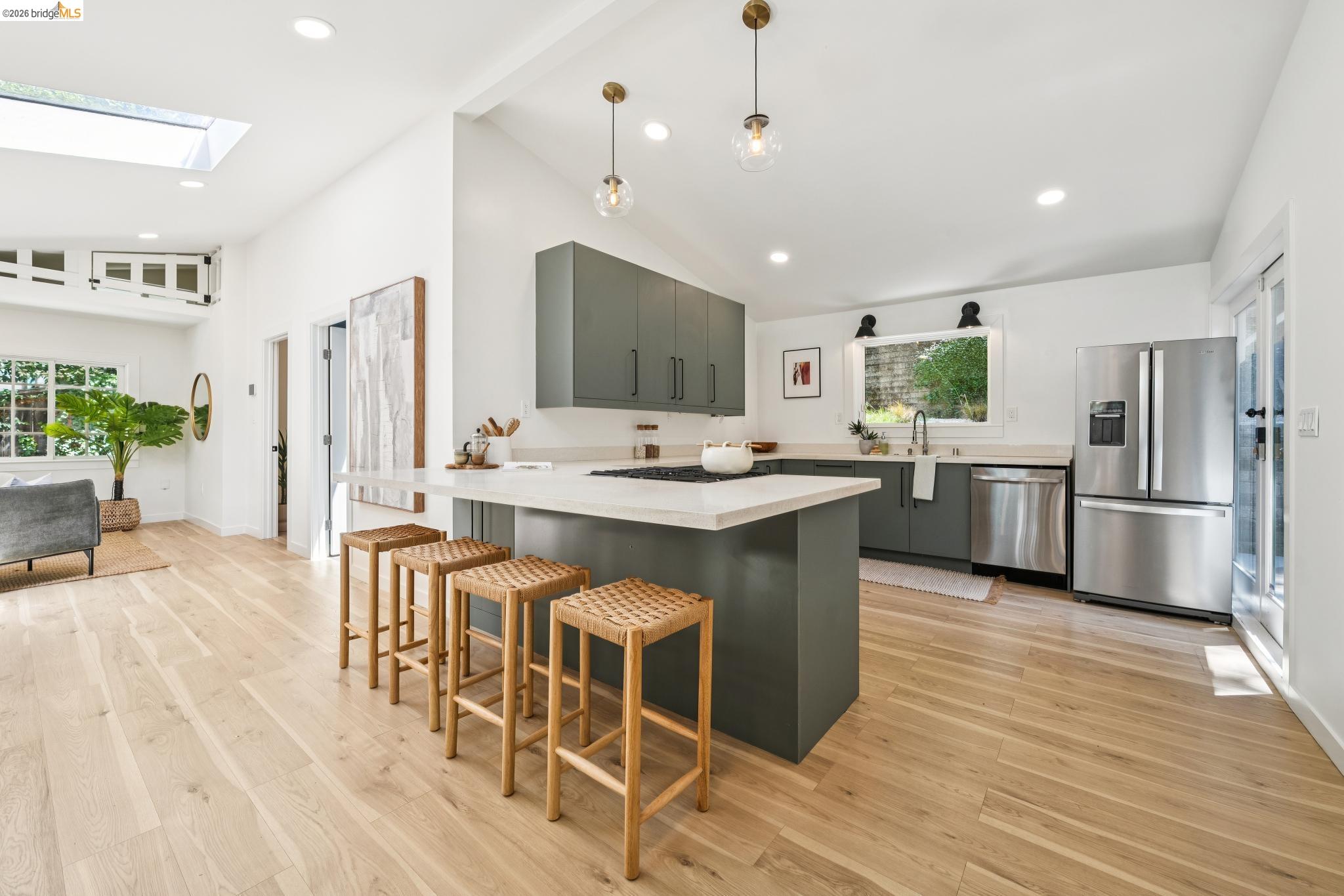 6400 Pinehaven Road Oakland, CA 94611 - Photo 23 of 78 Expansive kitchen featuring a central island with countertop seating, stainless steel appliances, dark green cabinetry, and wood-finish flooring