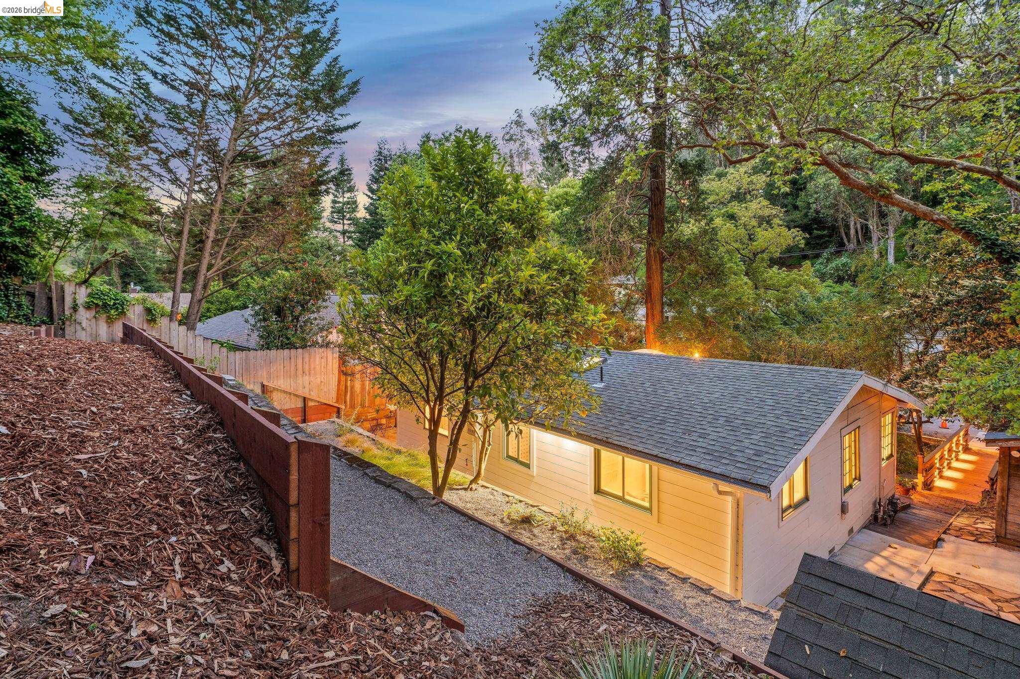 6400 Pinehaven Road Oakland, CA 94611 - Photo 72 of 78 Exterior property featuring a light-colored facade, dark shingle roof, and multiple windows with interior illumination