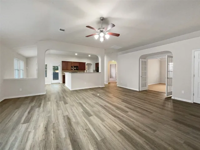 a view of an empty room with wooden floor and a kitchen