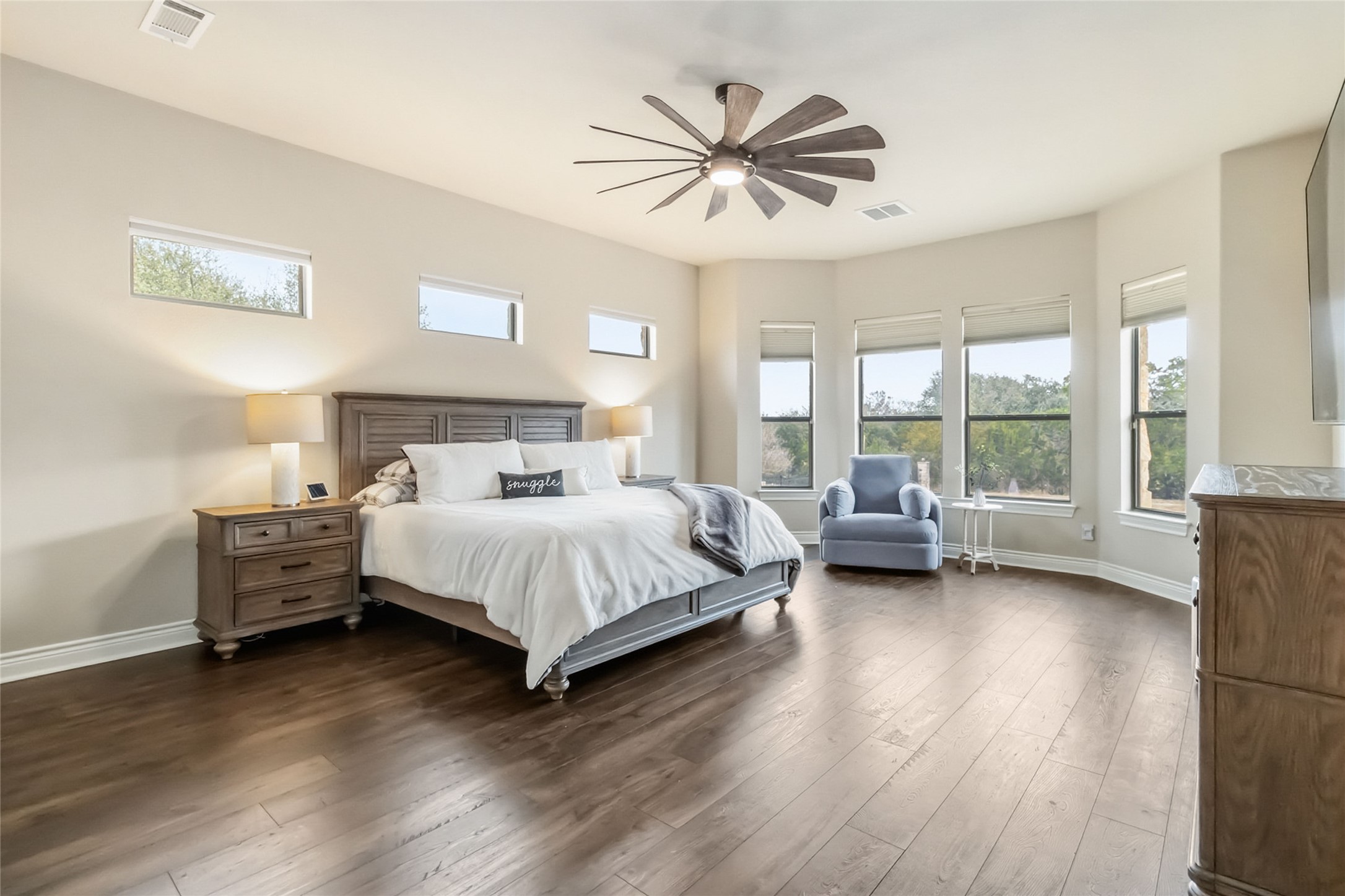 108 Standing Oak Drive Georgetown, TX 78633 - Photo 20 of 37 Spacious primary suite with rich LVP flooring, tray ceiling, and a modern ceiling fan creates a calm, inviting retreat. Abundant natural light pours in through multiple windows, offering peaceful views and a bright, airy feel.