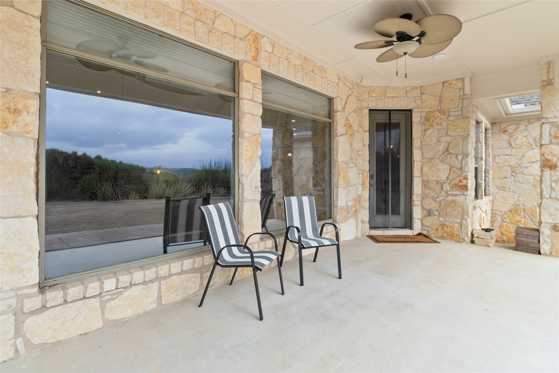 108 Standing Oak Drive Georgetown, TX 78633 - Photo 32 of 37 Covered back porch with stone exterior, ceiling fan, and oversized windows overlooking the backyard, ideal for relaxing or outdoor seating.