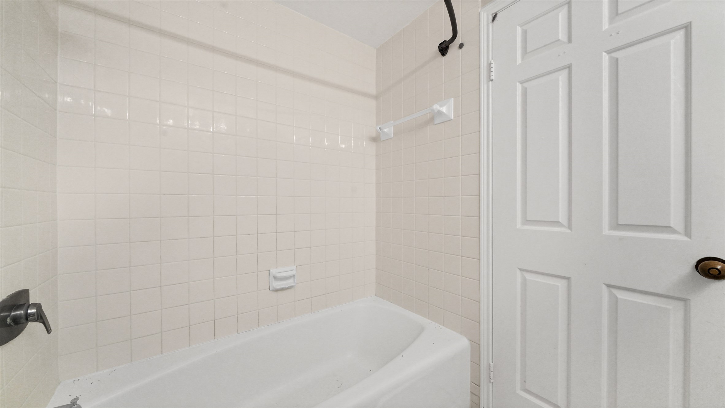 2001 Holcombe Boulevard, Unit 404 Houston, TX 77030 - Photo 12 of 33 This photo shows a bathroom featuring a white bathtub with cream-colored tile walls. The space includes a wall-mounted faucet and a white, paneled door.