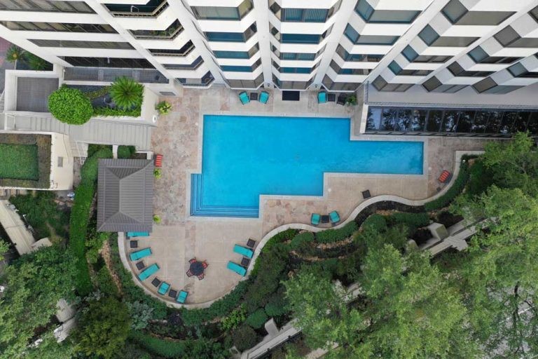 2001 Holcombe Boulevard, Unit 404 Houston, TX 77030 - Photo 19 of 33 This aerial view showcases a modern high-rise building with a large, inviting swimming pool surrounded by a spacious patio. The area features ample lounge chairs and landscaped greenery, providing a relaxing outdoor space for residents.