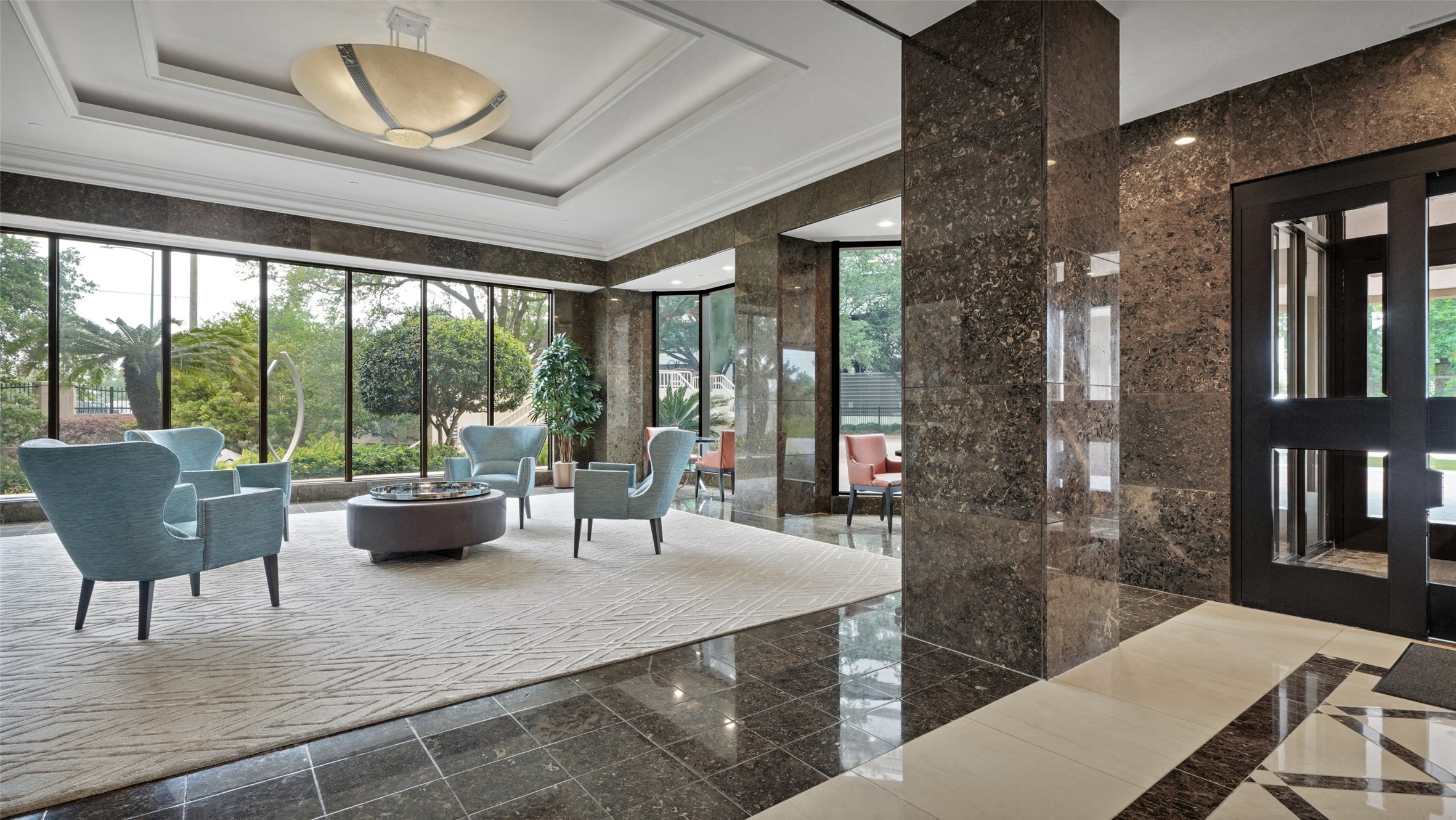 2001 Holcombe Boulevard, Unit 404 Houston, TX 77030 - Photo 20 of 33 This elegant lobby features floor-to-ceiling windows, allowing for abundant natural light and views of lush greenery. It offers a modern seating area with stylish chairs and a central table, set against polished marble floors and columns.