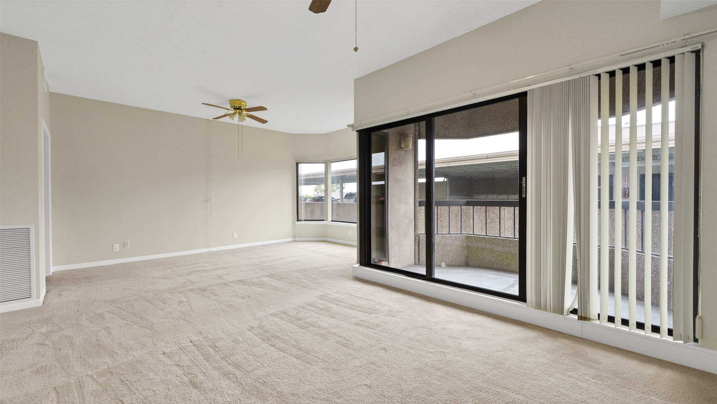 2001 Holcombe Boulevard, Unit 404 Houston, TX 77030 - Photo 3 of 33 Spacious, carpeted living room with neutral tones, featuring large sliding glass doors leading to a balcony. Ample natural light streams through vertical blinds, and a ceiling fan adds comfort.