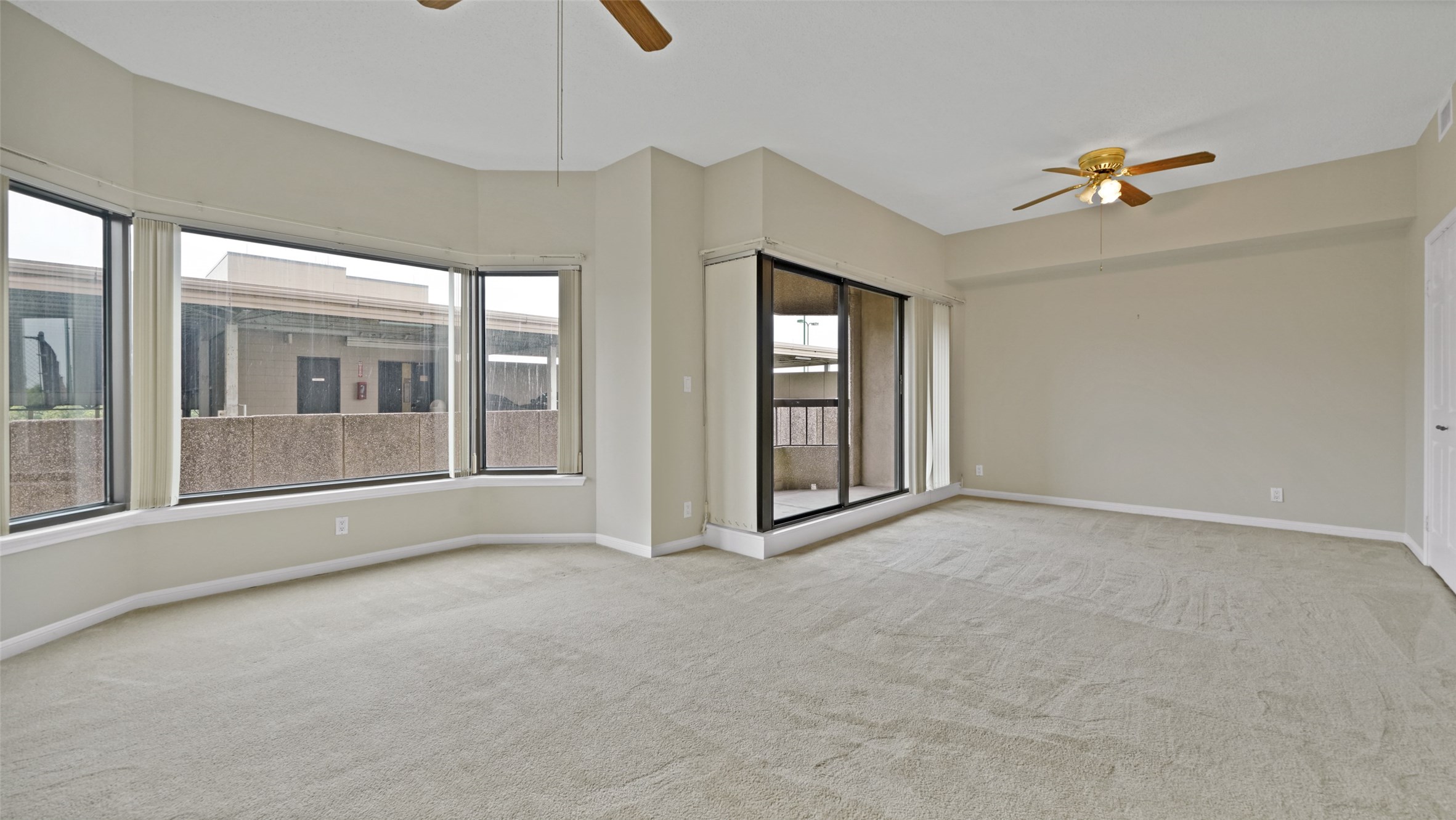 2001 Holcombe Boulevard, Unit 404 Houston, TX 77030 - Photo 30 of 33 Spacious, light-filled room with large windows and a sliding glass door leading to a balcony. Features neutral carpeting, ceiling fan, and plenty of natural light, perfect for a living area or bedroom.