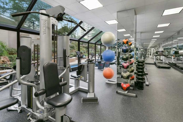 2001 Holcombe Boulevard, Unit 404 Houston, TX 77030 - Photo 32 of 33 This photo showcases a spacious, well-equipped gym with large windows offering natural light and a view of greenery. It features various exercise machines, free weights, and fitness balls, providing a comprehensive workout environment.