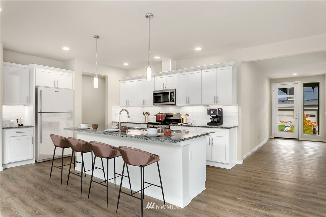 309 Southwest 3rd Court, Unit 9 Renton, WA 98057 - Photo 7 of 25 a kitchen with stainless steel appliances kitchen island granite countertop a stove a sink a refrigerator and white cabinets with wooden floor