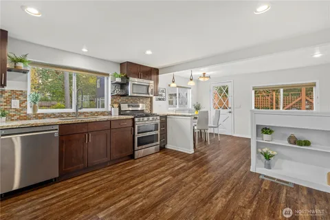 a kitchen with stainless steel appliances granite countertop wooden cabinets a stove top oven a sink and dishwasher a dining table with wooden floor