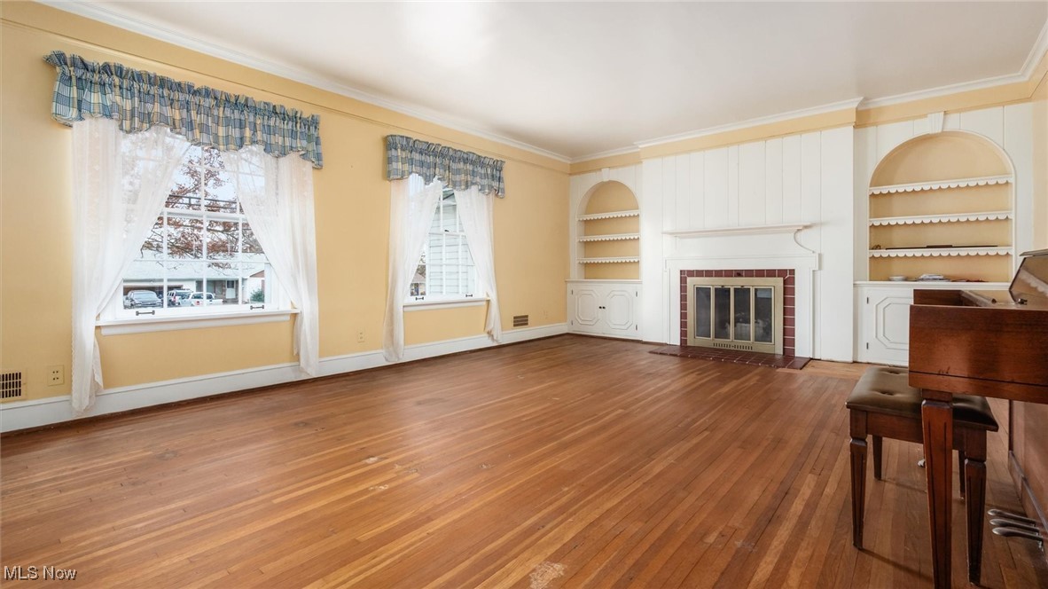 Unfurnished living room with built in features, hardwood / wood-style floors, a fireplace, and ornamental molding
