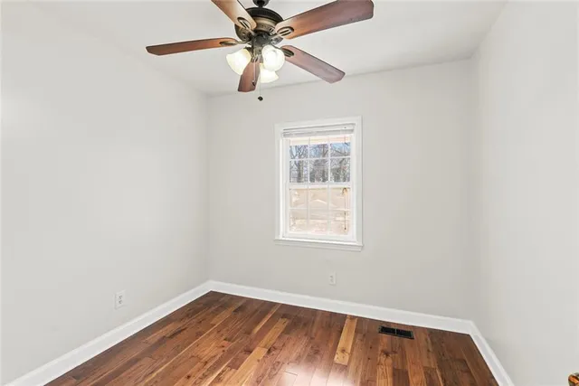 an empty room with wooden floor fan and windows