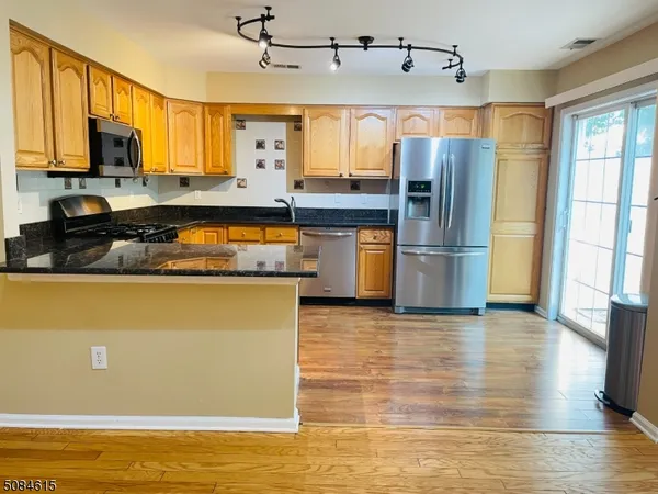 a kitchen with stainless steel appliances granite countertop a refrigerator a stove top oven and a sink with wooden floor