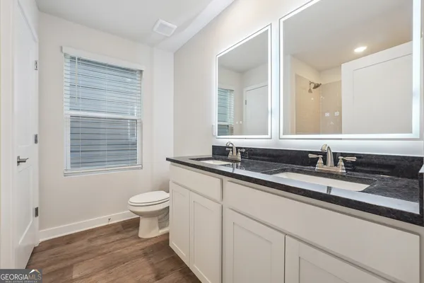 a bathroom with a granite countertop sink a toilet a mirror and a window