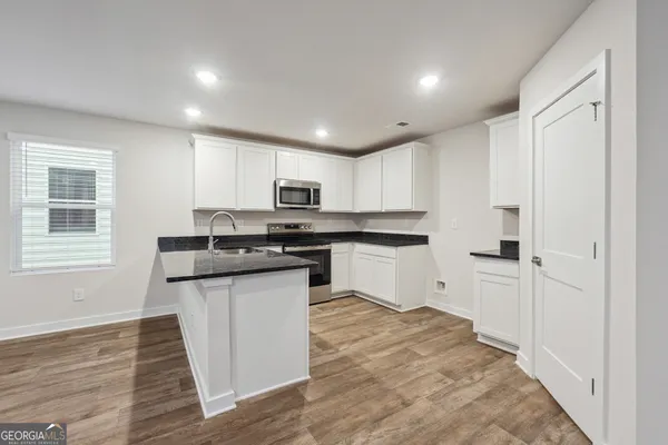 a kitchen with stainless steel appliances granite countertop a refrigerator a sink dishwasher a stove and white countertops with wooden floor