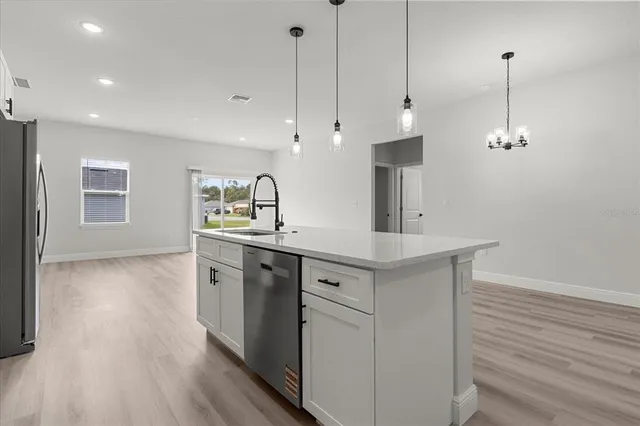 a kitchen with stainless steel appliances granite countertop a sink a stove a refrigerator and white cabinets with wooden floor