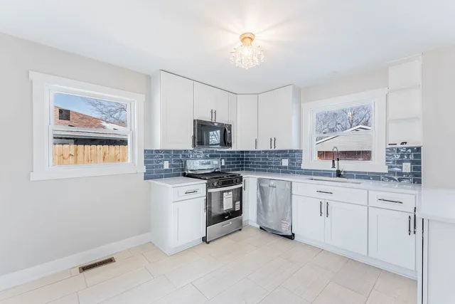 a kitchen with granite countertop white cabinets a sink a stove a dining table and chairs