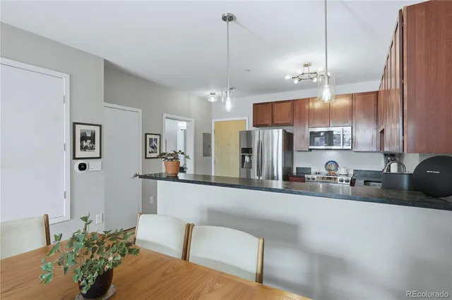 a kitchen with stainless steel appliances kitchen island granite countertop a refrigerator a sink a dining table and chairs with wooden floor