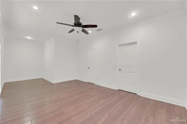 an empty room with wooden floor ceiling fan and windows
