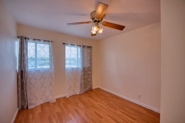 an empty room with wooden floor fan and windows