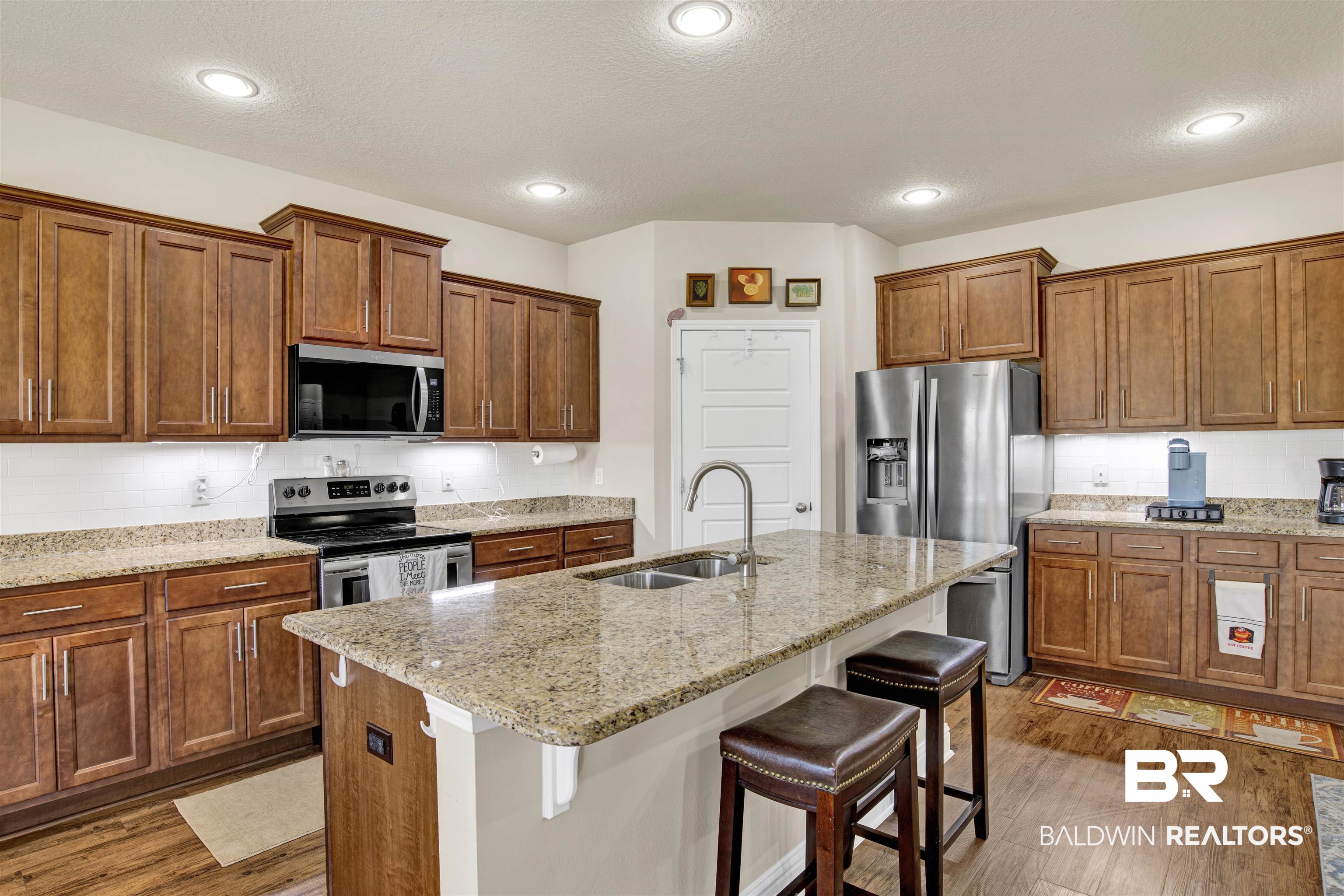 278 Silo Loop Fairhope, AL 36532 - Photo 7 of 26 Kitchen featuring stainless steel appliances, wood finished floors, a kitchen bar, brown cabinetry, and a textured ceiling