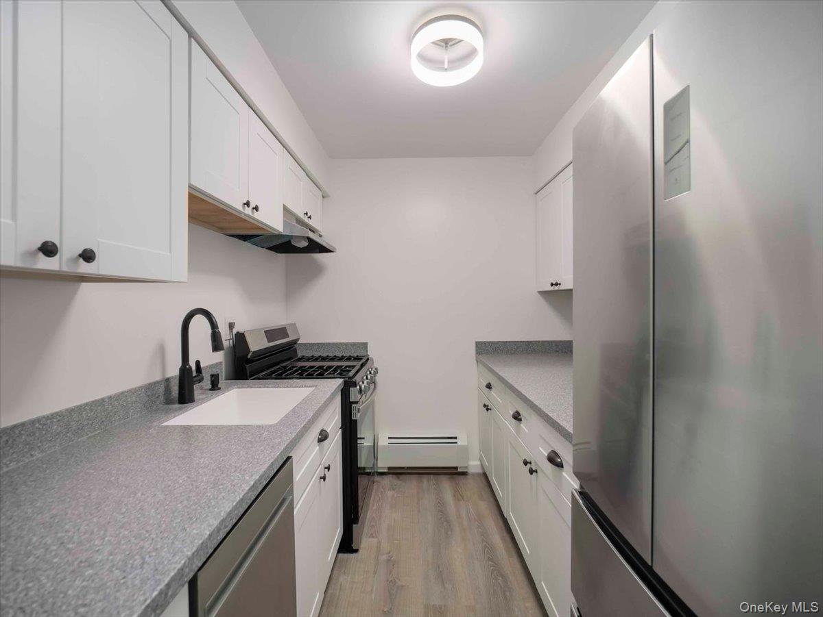 27 Tanager Road, Unit 2702 Monroe, NY 10950 - Photo 10 of 35 Galley kitchen featuring white shaker cabinetry, speckled countertops, stainless steel appliances, and wood-finish flooring